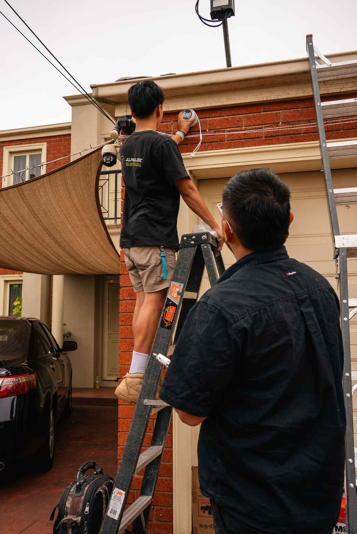 Alphalink apprentice on a ladder installing a camera while Jimmy supervises